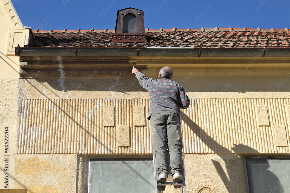 Renovation, senior worker at ladder painting old house facade Renovation, senior worker at ladder painting old house facade