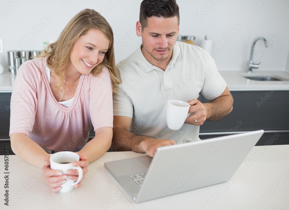 Couple with coffee cups using laptop at table Couple with coffee cups using laptop at table