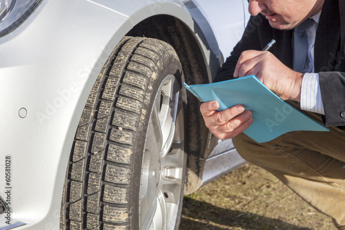 Man with paper block kneeling on car tires