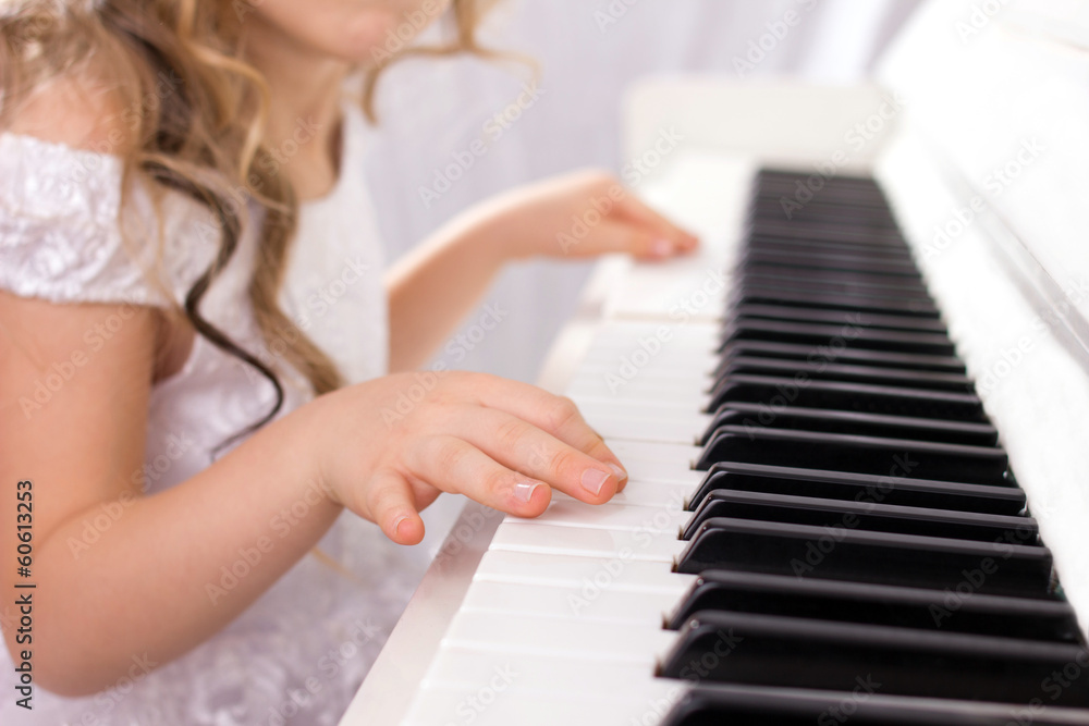 Fototapeta premium little girl in white dress playing on white piano, close-up