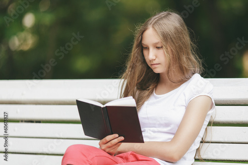 young teenage girl reading book on bench