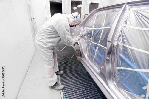 auto mechanic spraying paint on a car in a special booth