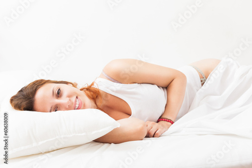Long-haired woman lying on white sheet in bed at home