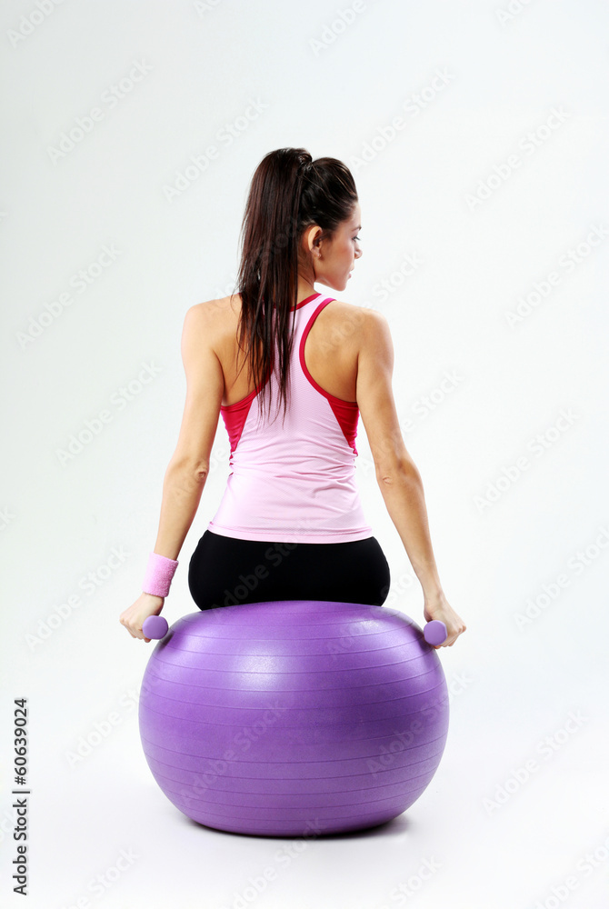 woman sitting on fitball with dumbells on gray background woman sitting on fitball with dumbells on gray background