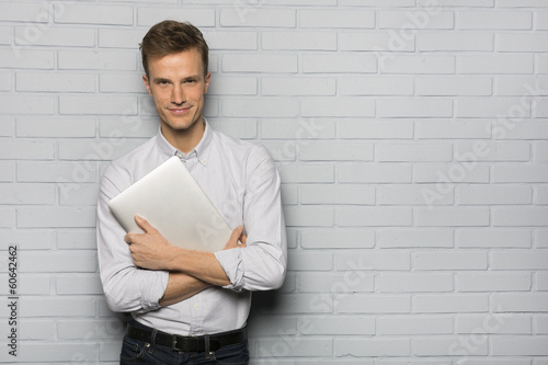 Tableau sur toile Handsome Cheerful man holding a laptop, isolated over a wall