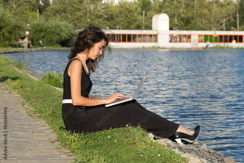 Девушка сидит на берегу пруда с ноутбуком
