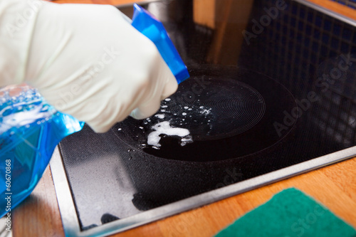 Person's Hand Spraying Liquid On Induction Cooker photo