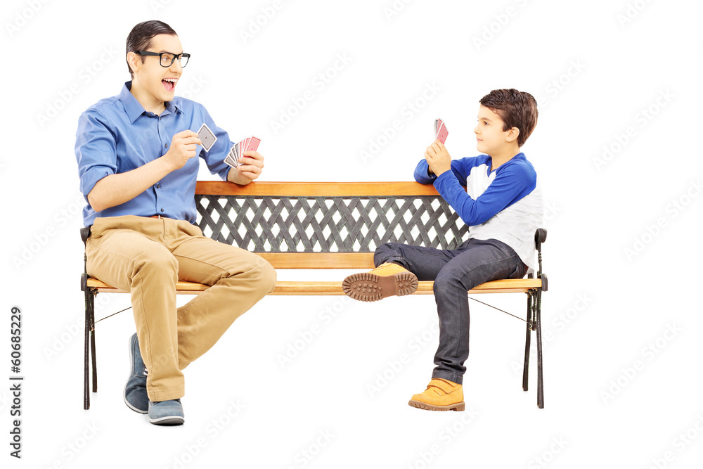 Young boy playing cards with his older cousin seated on bench