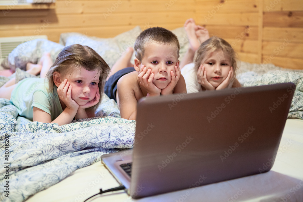Three children looking at laptop monitor while laying in bed Three children looking at laptop monitor while laying in bed
