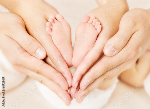 Fototapeta Naklejka Na Ścianę i Meble -  Newborn baby feet in parents hands. Love simbol as heart sign