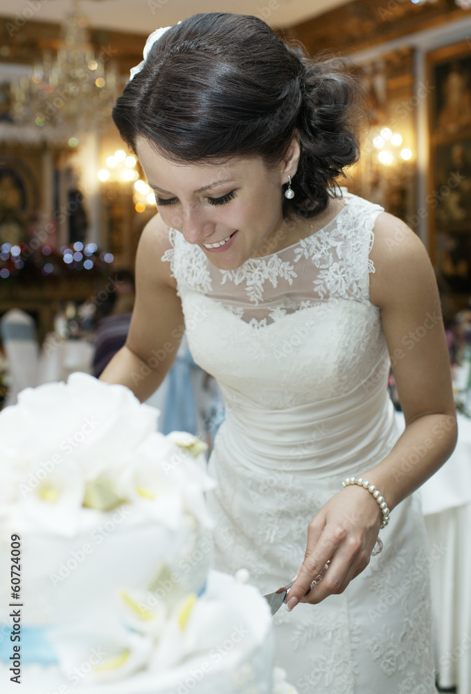 Fototapeta premium Smiling beautiful bride cutting the wedding cake