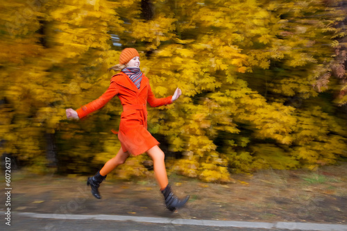 Girl in orange coat running in the yellow autumn forest.