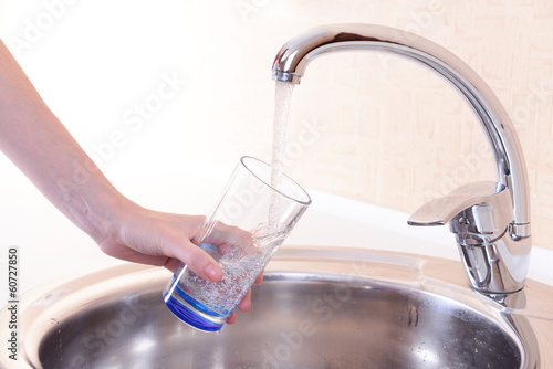 Hand holding glass of water poured from kitchen faucet