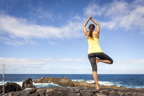 Young woman practicing tree yoga pose near the ocean