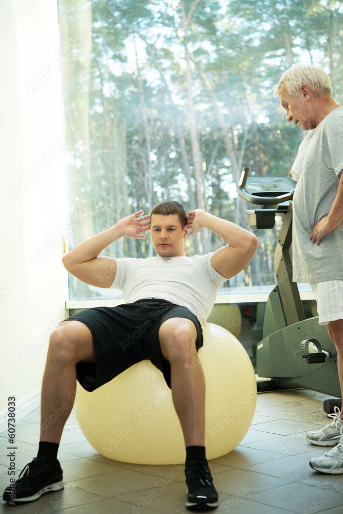 Obraz premium Personal trainer shows to a senior man how to do exercise 