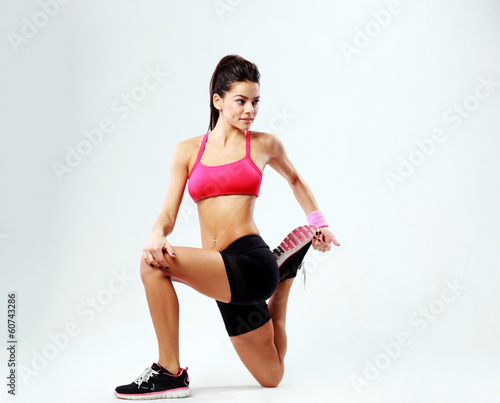 Young beautiful sport woman stretching legs on gray background