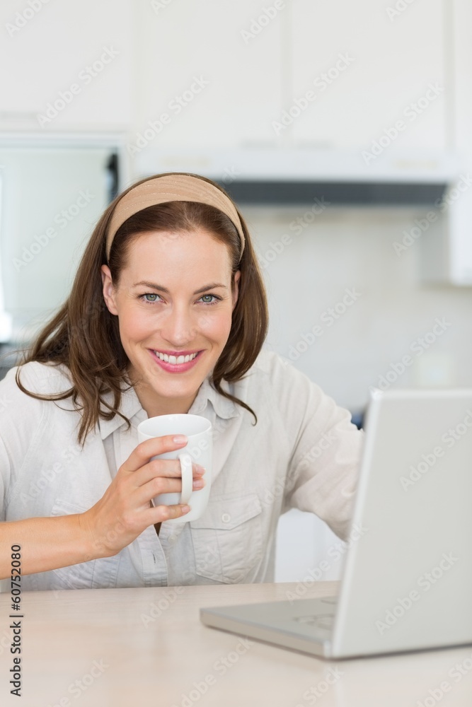 Smiling woman with coffee cup and laptop in kitchen Smiling woman with coffee cup and laptop in kitchen