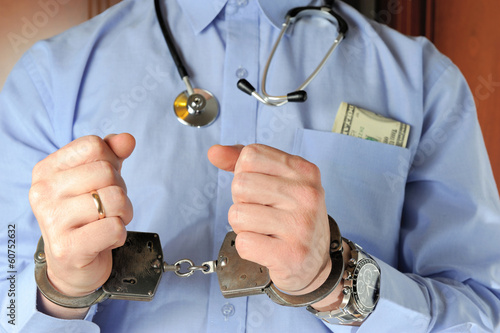 Man with stethoscope holds his hands in handcuffs before itself