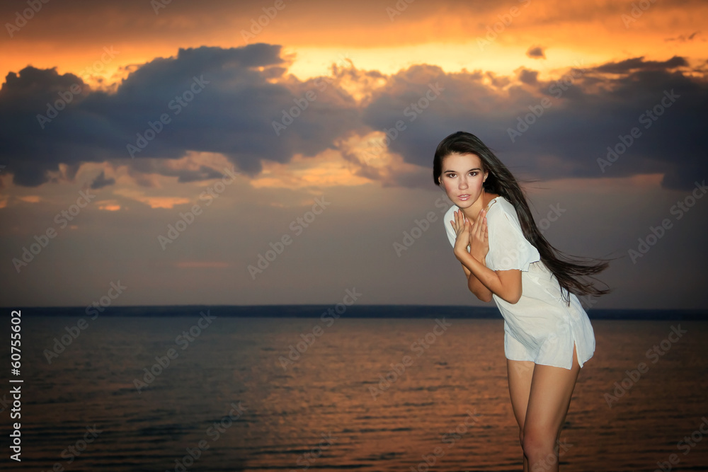 Pretty female standing near ocean in rays of sunset