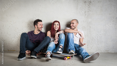 Happy friends portrait with skateboard against concrete wall.