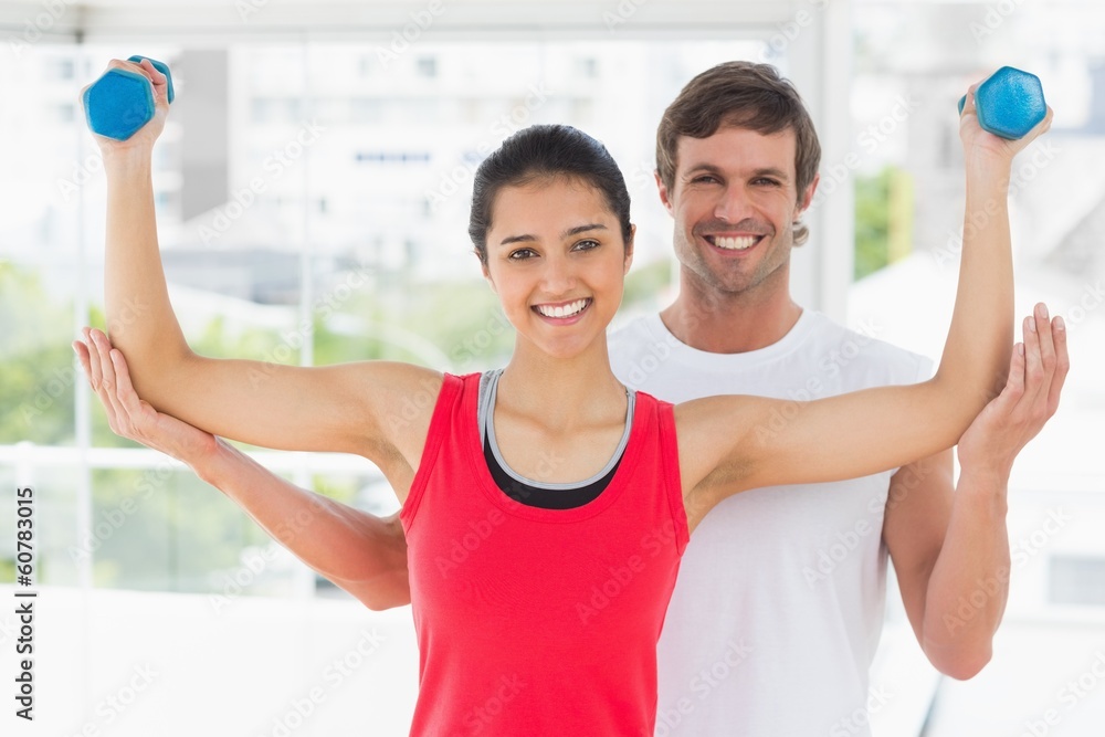 Smiling instructor with woman lifting dumbbell weights
