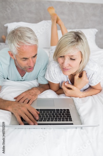 Mature couple using laptop in bed