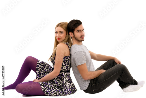Cheerful young couple sitting with back to each other on floor,