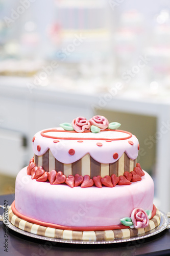 Wedding cake decorated with pink rose flowers and hearts .