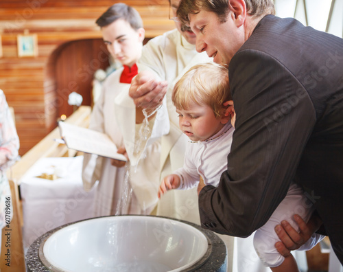 Obraz na plátne Little baby boy being baptized in catholic church holding by fat