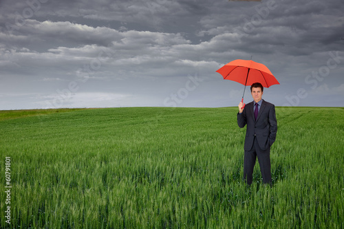 Business man with umbrella in green field