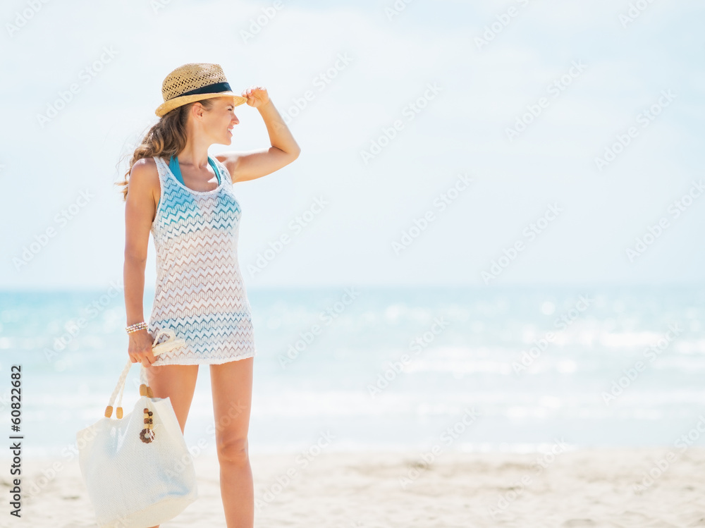 Full length portrait of young woman in hat and with bag on beach