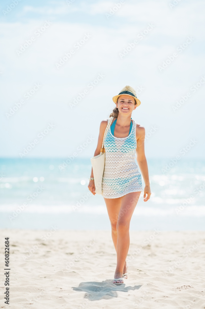 Young woman in hat and with bag walking on beach