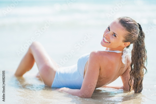 Smiling young woman in swimsuit laying at seaside. rear view