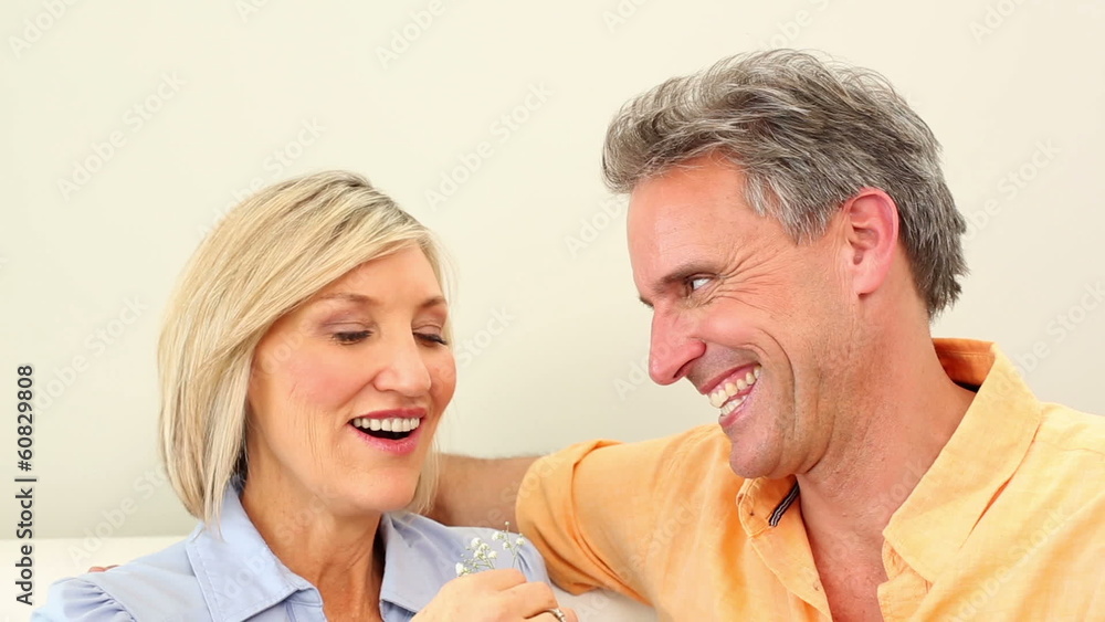 Husband giving his wife a small flower on the couch Husband giving his wife a small flower on the couch
