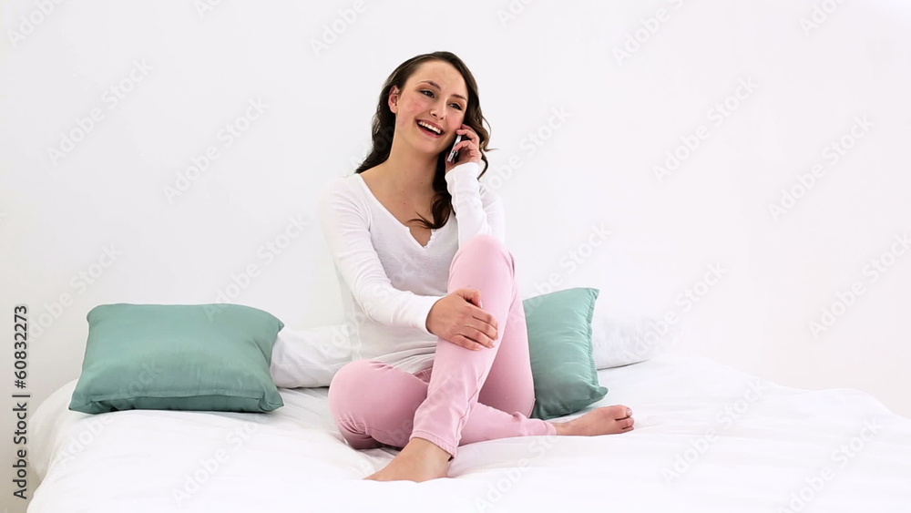 Smiling woman sitting on bed talking on the phone Smiling woman sitting on bed talking on the phone