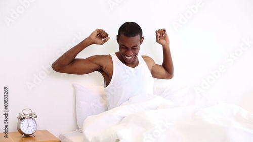 Smiling man yawning and stretching sitting in bed