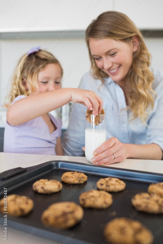 Mother with daughter dipping cookie in milk Mother with daughter dipping cookie in milk