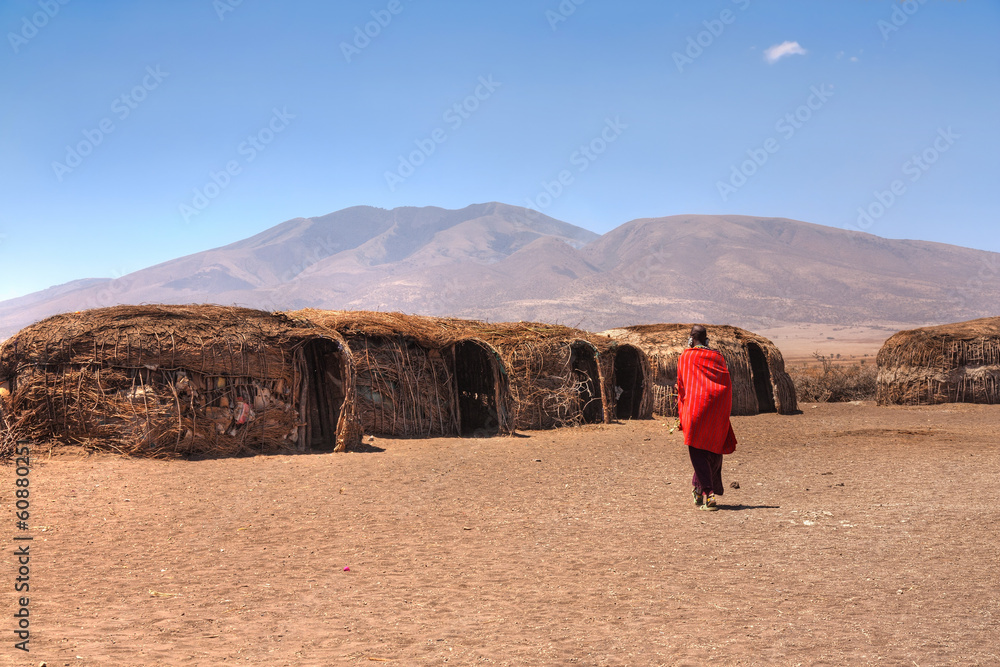 Massai huts with a woman in red in back view