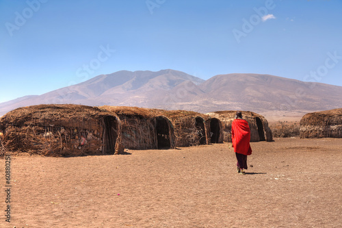 Massai huts with a woman in red in back view photo