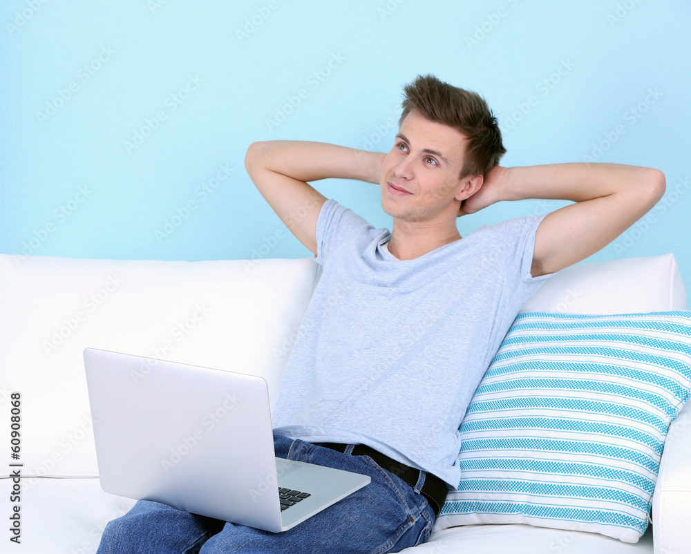 Guy sitting on sofa with laptop on blue background Guy sitting on sofa with laptop on blue background