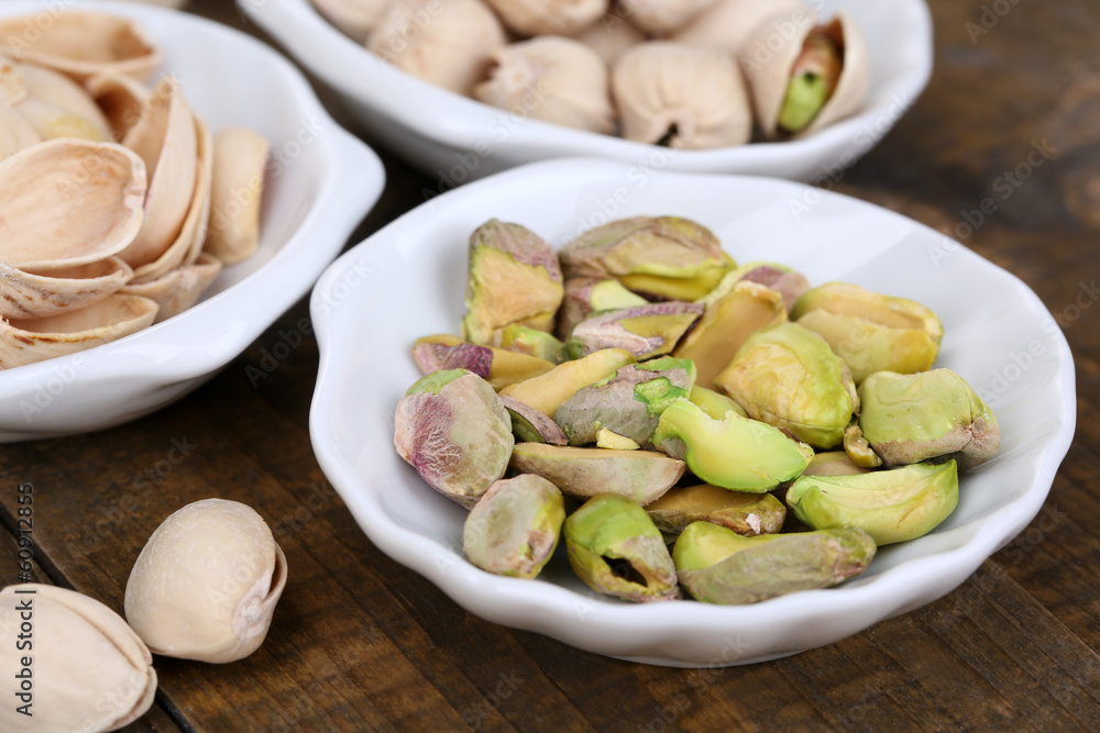 Pistachio nuts in small bowls on wooden background Pistachio nuts in small bowls on wooden background