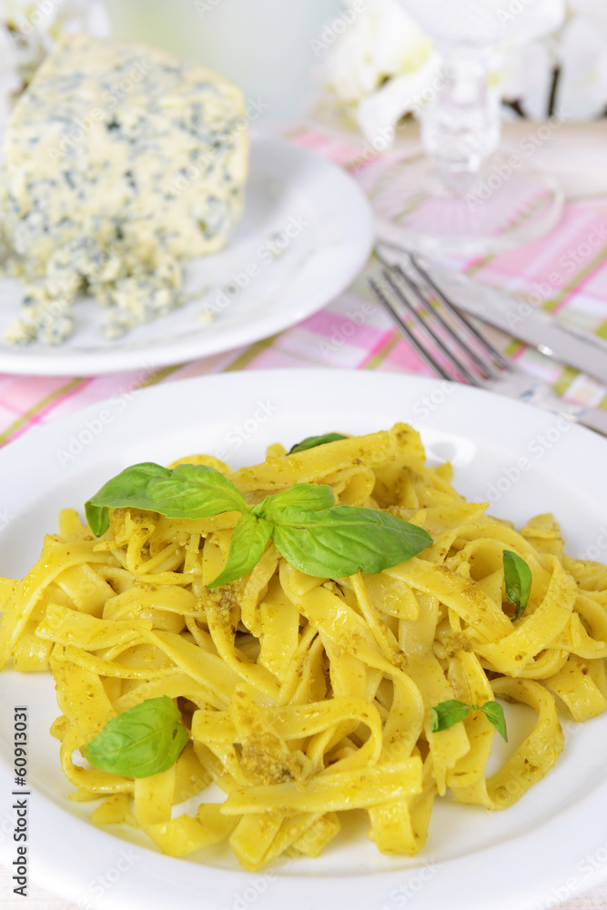 Delicious pasta with pesto on plate on table on light Delicious pasta with pesto on plate on table on light