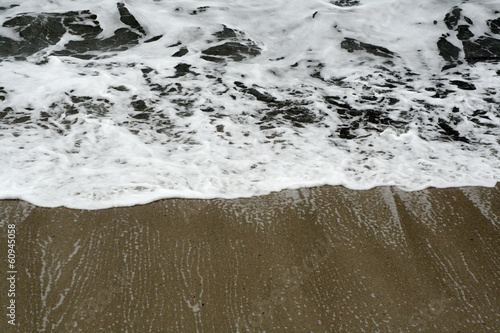 white sea waves crashing and receding on sandy beach photo