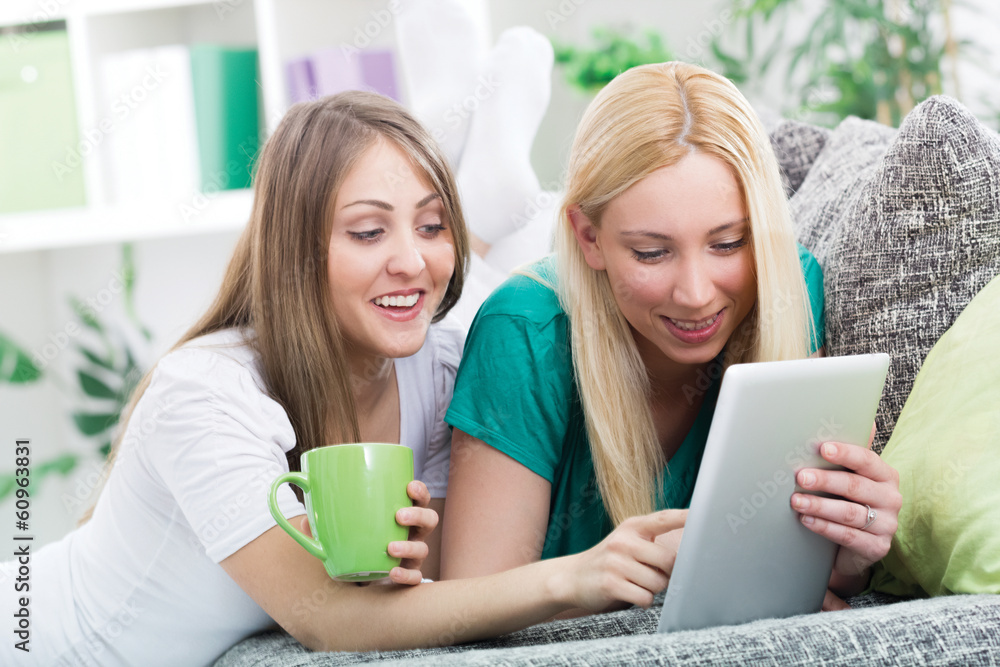two happy young woman with digital tablet relaxing in room two happy young woman with digital tablet relaxing in room