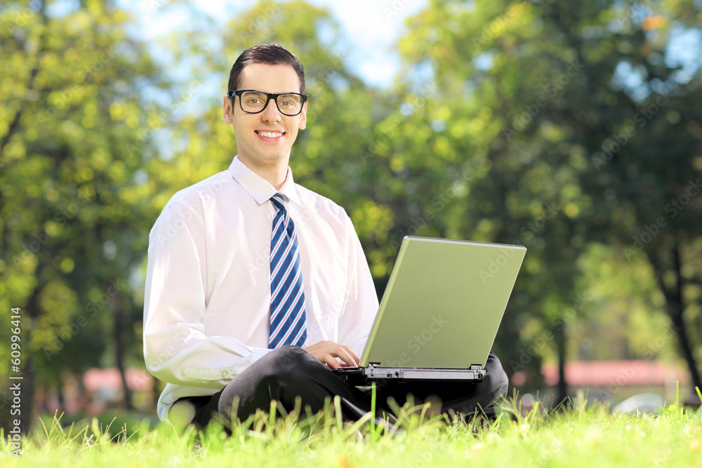 Young businessman sitting on a grass and working on a laptop Young businessman sitting on a grass and working on a laptop