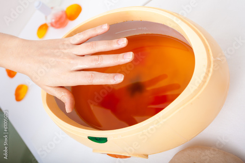 Canvas Print Female hand and orange paraffin wax bowl. Woman in beauty salon