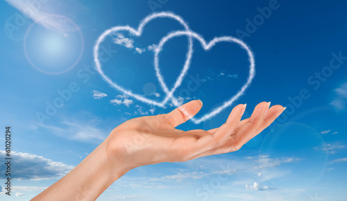 woman hand and heart shaped clouds on blue sky background photo