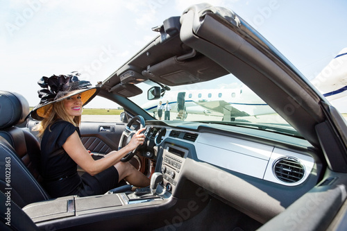 Woman Driving Convertible Towards Private Jet At Terminal