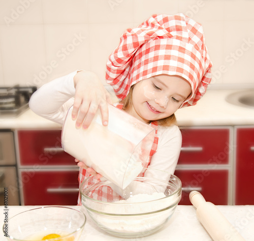 Smiling little girl with chef hat put flour for baking cookies photo