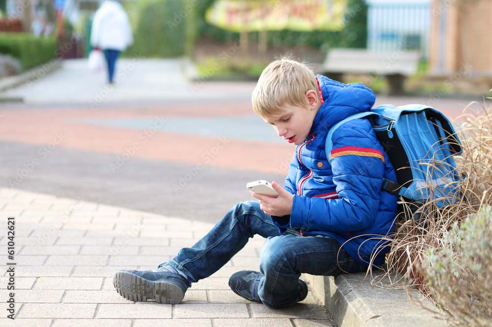 Teenager boy calling on mobile phone sitting outside of school Teenager boy calling on mobile phone sitting outside of school